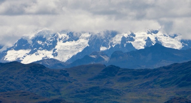 Snow-covered mountain peaks above vegetated slopes under cloudy skies